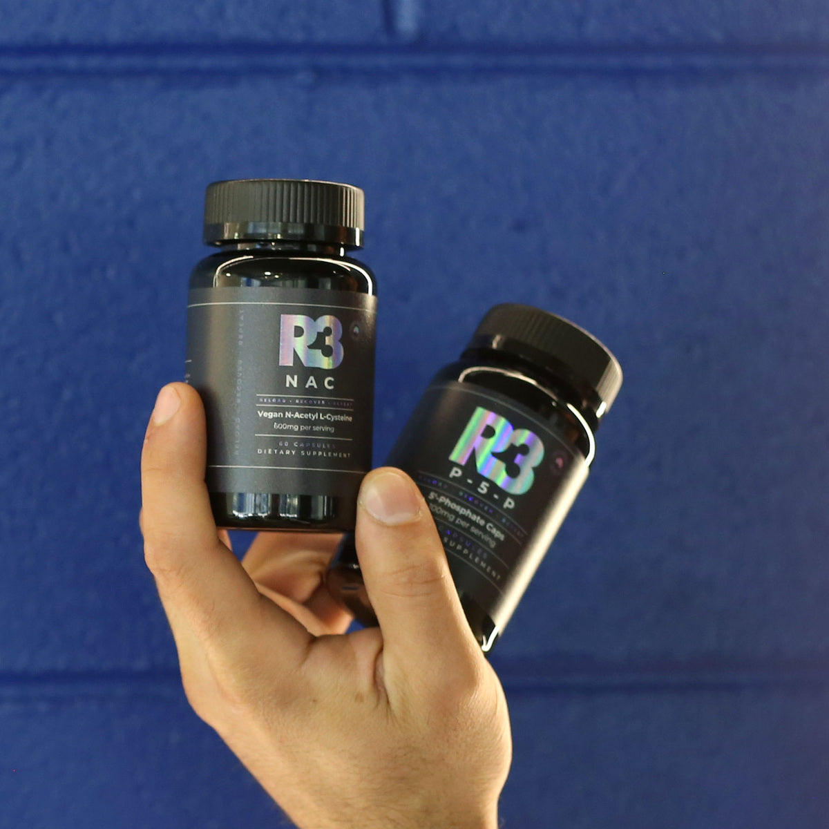 Two centred R3 capsule bottles against a navy wall