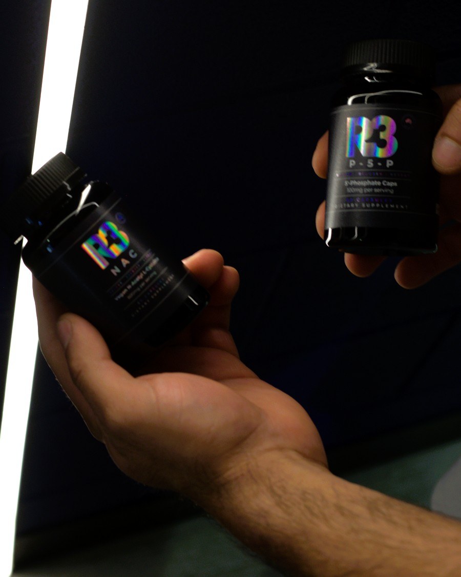Hand holding two R3 supplement bottles in a dark routine scene